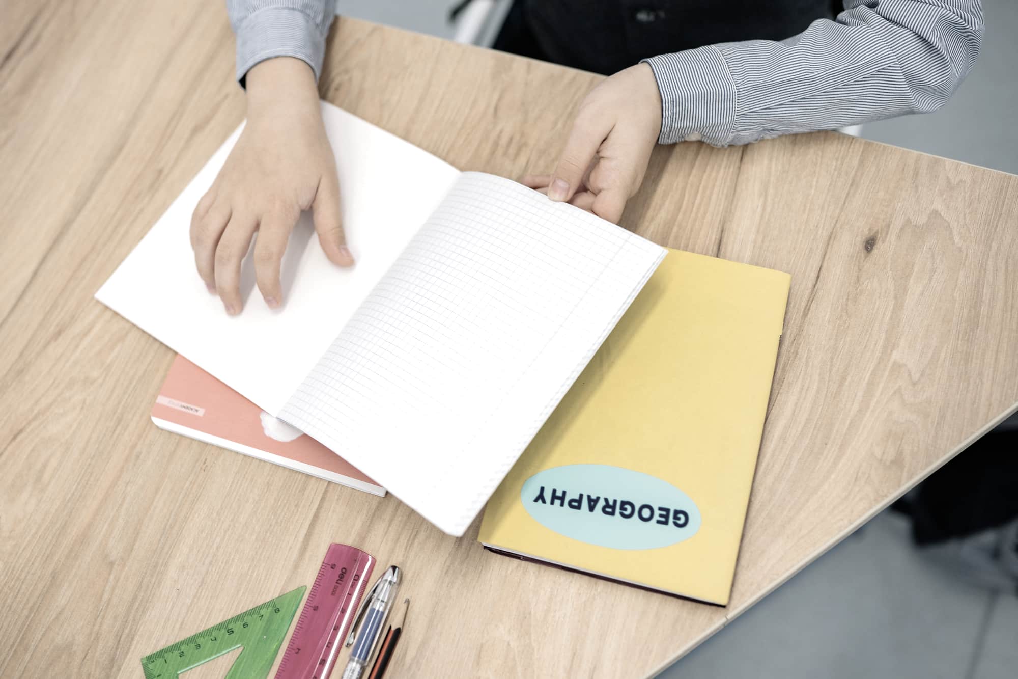 Hands turning the pages of a notebook on a wooden desk with pens