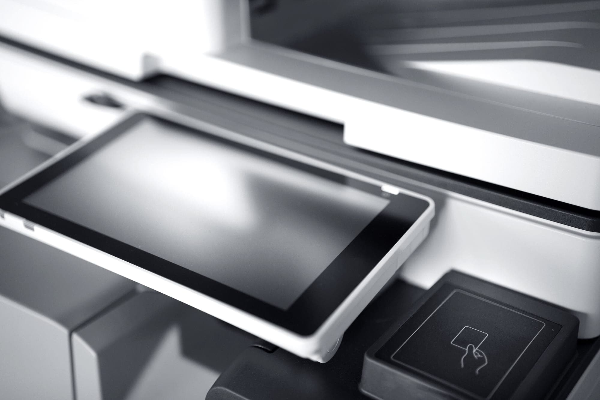 A modern office printer with a control panel against a light wall