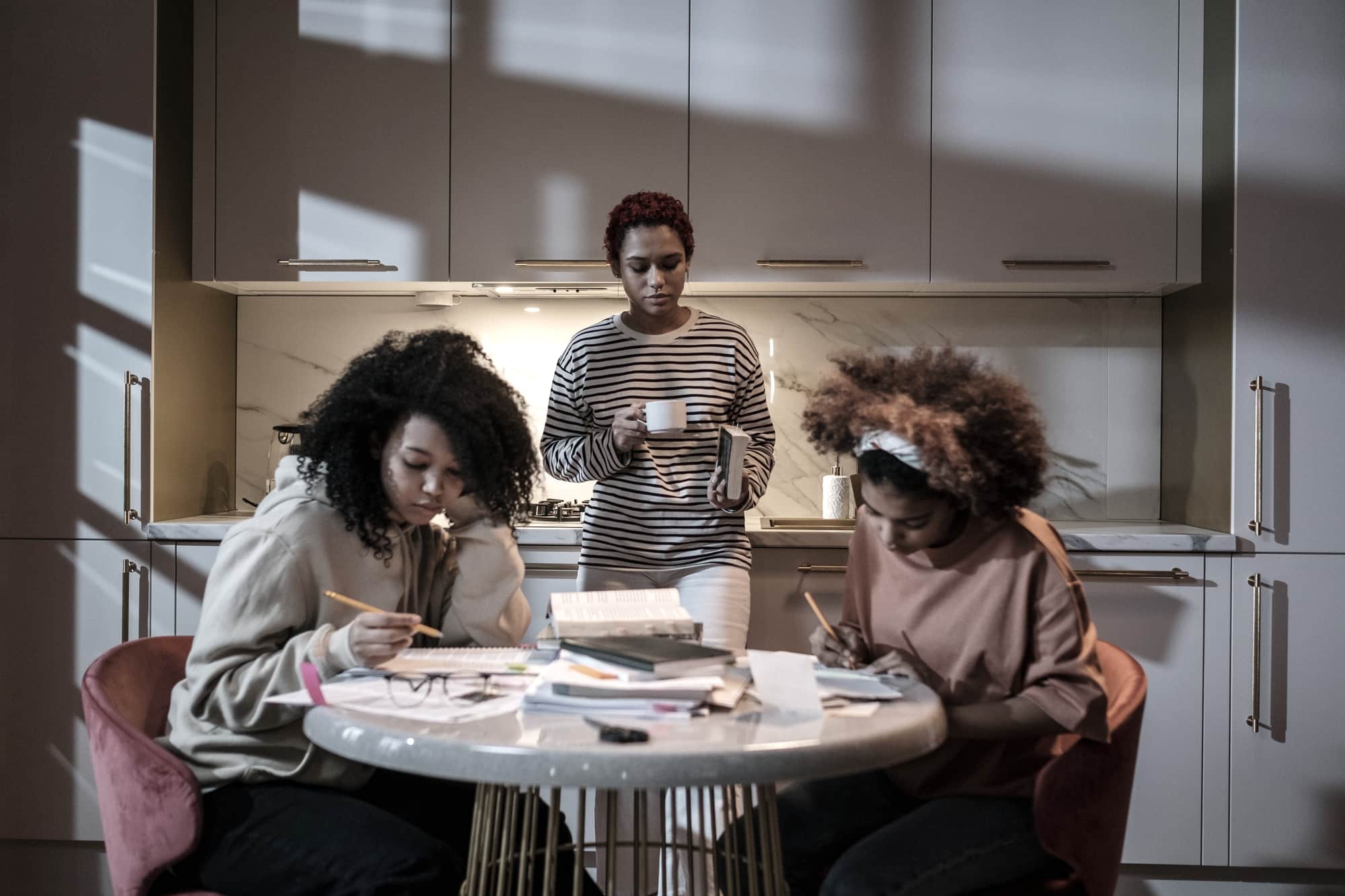 People studying at a kitchen table with papers and notebooks in daylight