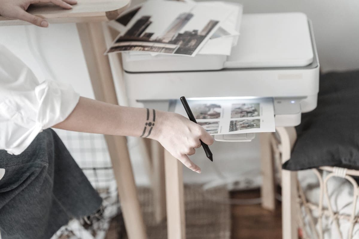 A person using a home inkjet printer at a desk beside printed sheets
