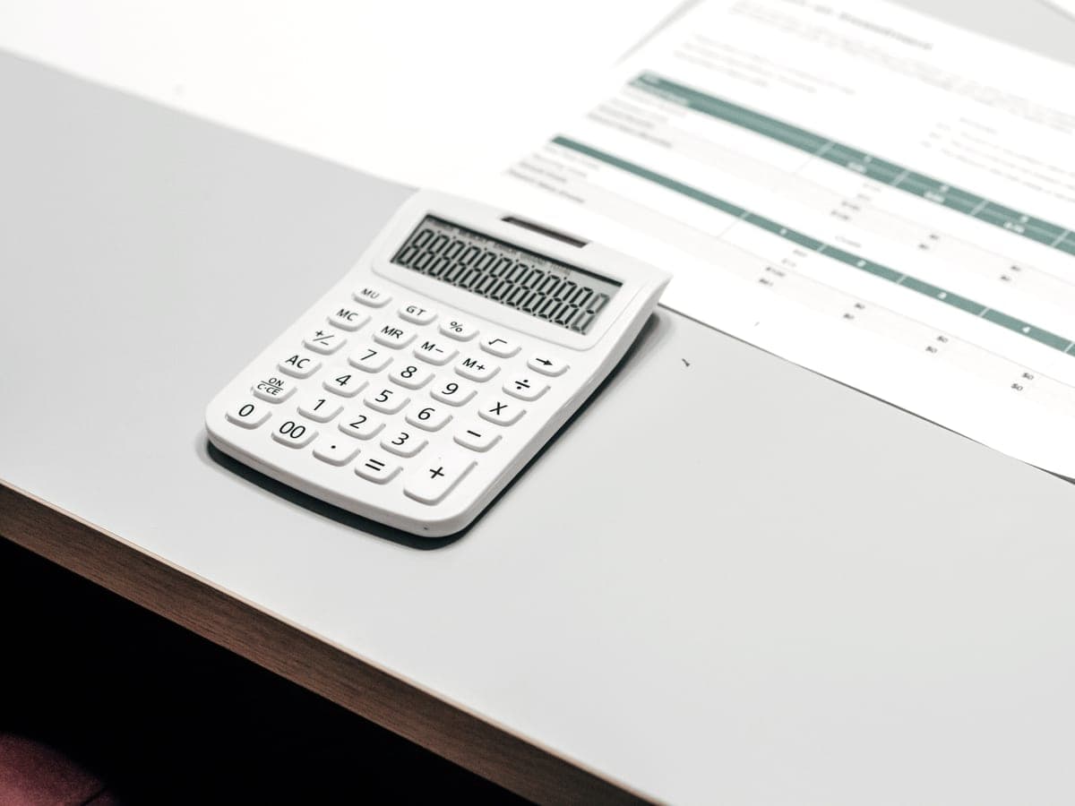 A white calculator beside a printed spreadsheet on a desk