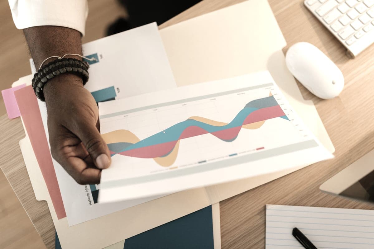 A hand holding a printed color business graph on a desk