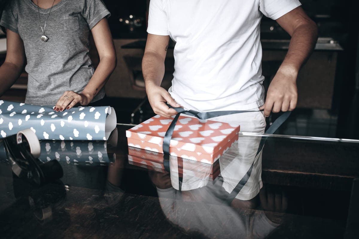 Two people wrapping a gift box in patterned paper
