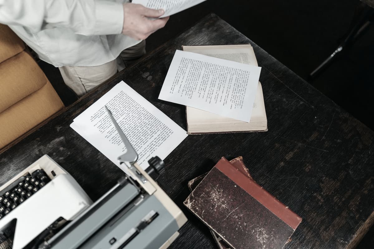 An overhead view of a wooden desk with a typewriter, papers and books
