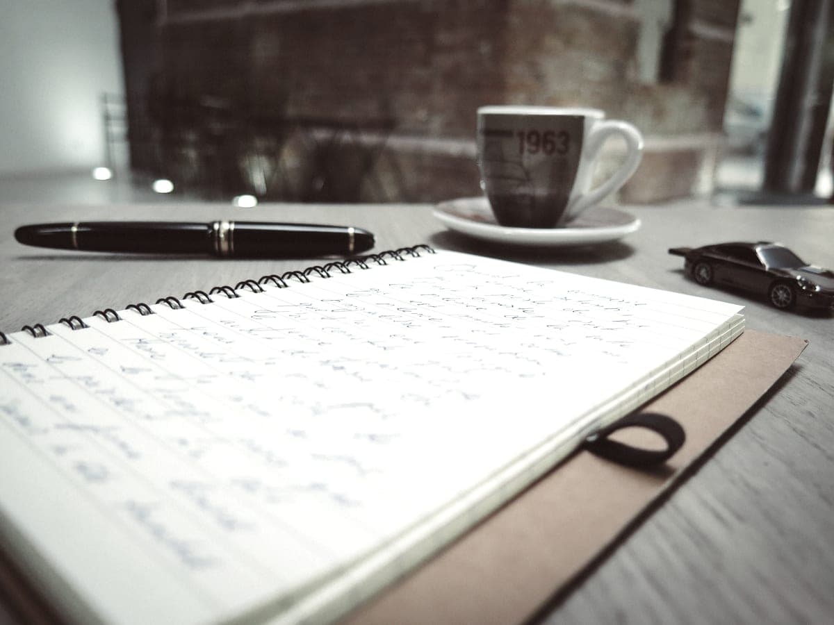 A spiral notepad and pen beside a coffee cup on a desk