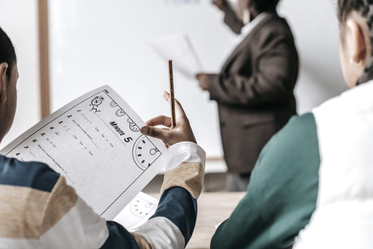A teacher standing beside pupils seated at their desks in a classroom