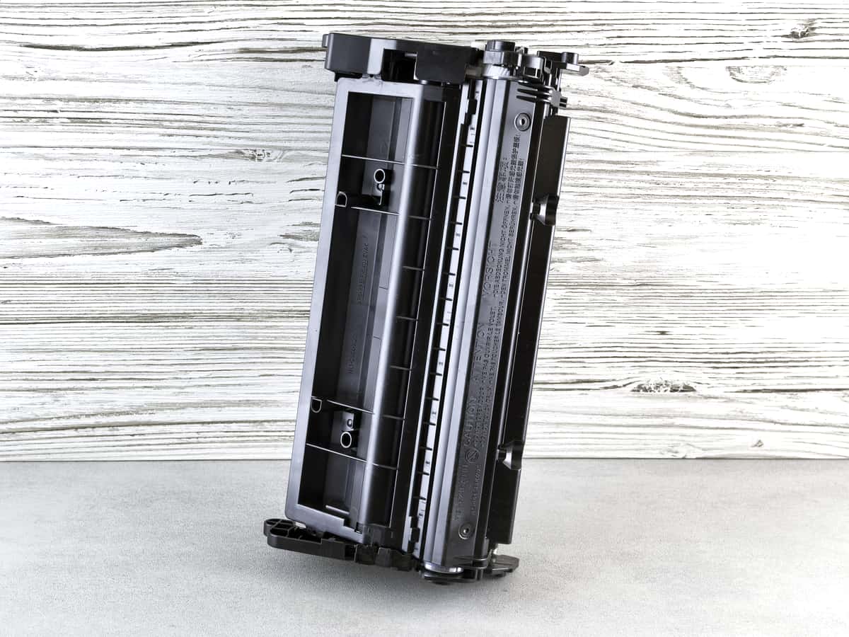 A black printer toner cartridge against a wooden background