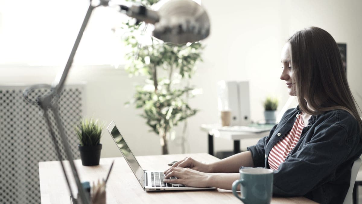 A person working at a laptop in a bright home office with plants